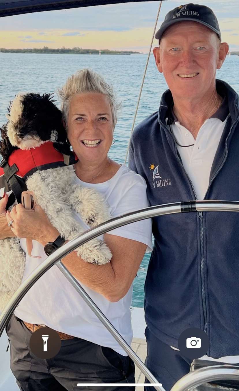 skipper and crew onboard sun sailing charter dog being held by crew with skipper onboard yacht